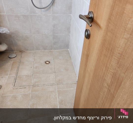 מקלחת עם אריחים חדשים ודלת עץ פתוחה